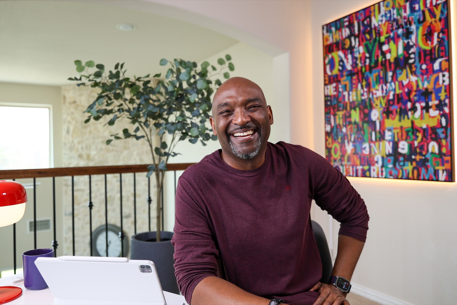 Ron Davis laughing at his desk in front of a colorful typography painting